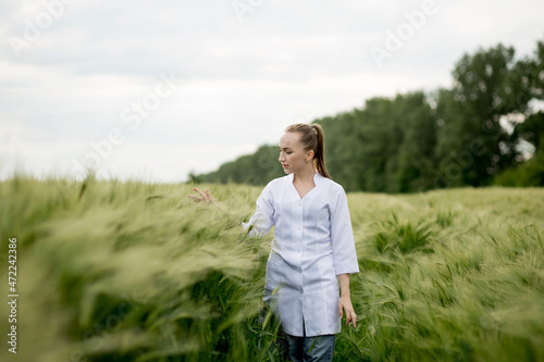 Young woman agronomist in white coat squatting in green wheat field and checking crop quality © volody10