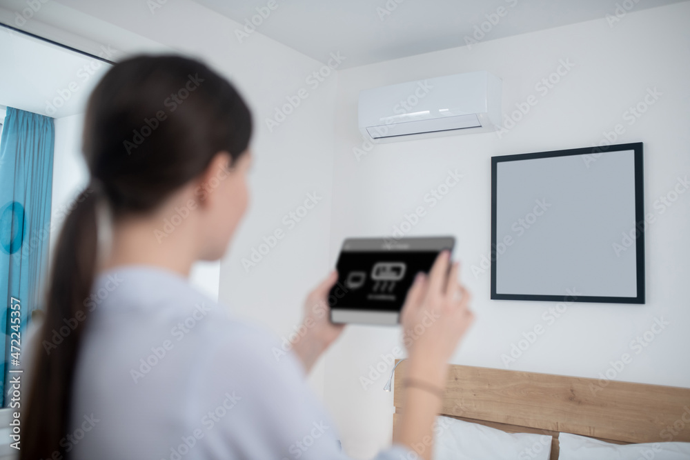 Woman turning on an air conditioner using a tablet Woman turning on an air conditioner using a tablet