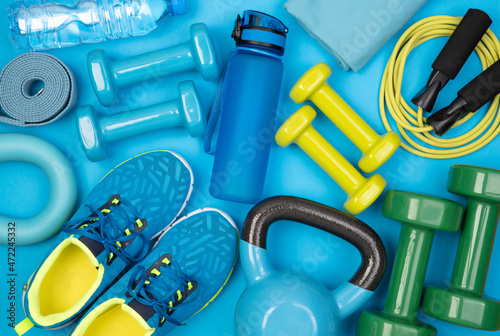 Dumbbells, trainers, jumping rope and other fitness equipment on blue background, top view