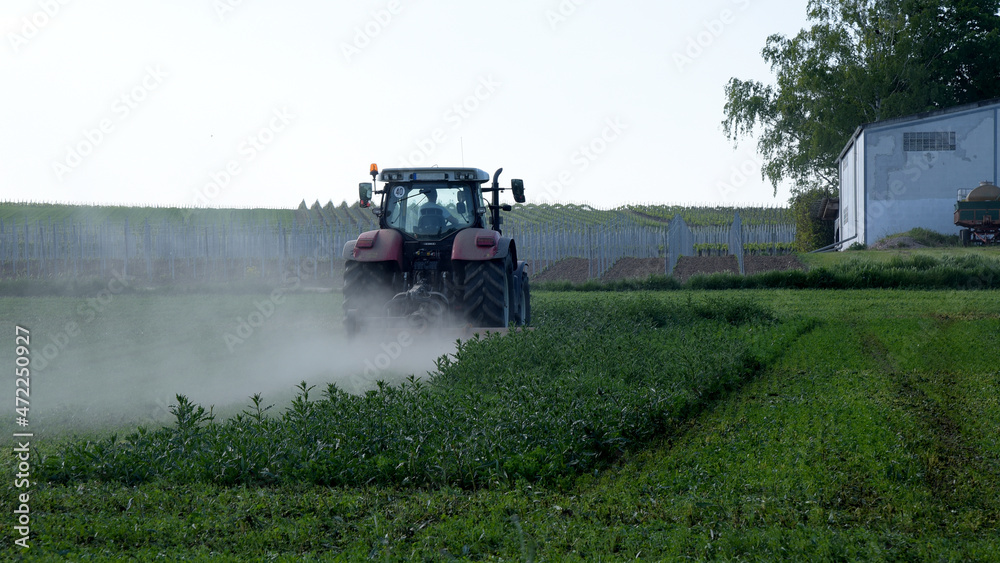 Fototapeta premium Tractor cultivating a field with a trail of dust