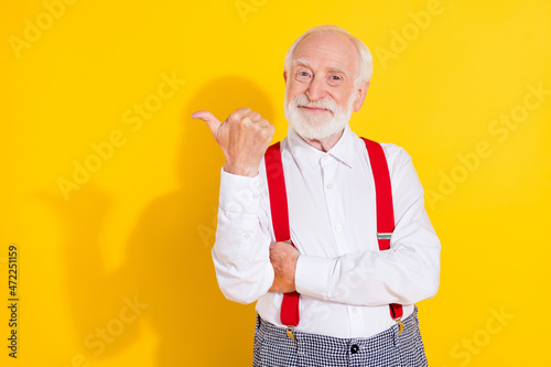 Photo of funnky old white hair man show ad wear white shirt suspenders isolated on yellow color background photo