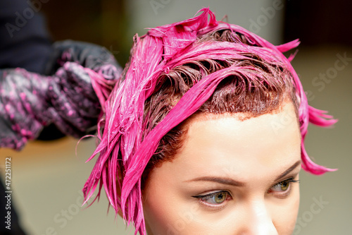 Fotografie The professional hairdresser uses a brush to apply the pink dye to the hair