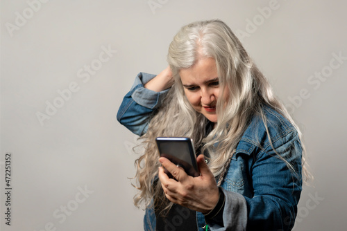Woman with white hair and blue denim jacket looking at mobile phone and fixing her hair