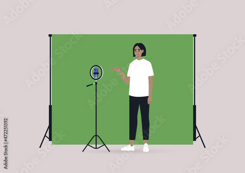 A young female Caucasian blogger recording a video with a tripod, a mobile phone, and a chroma key screen