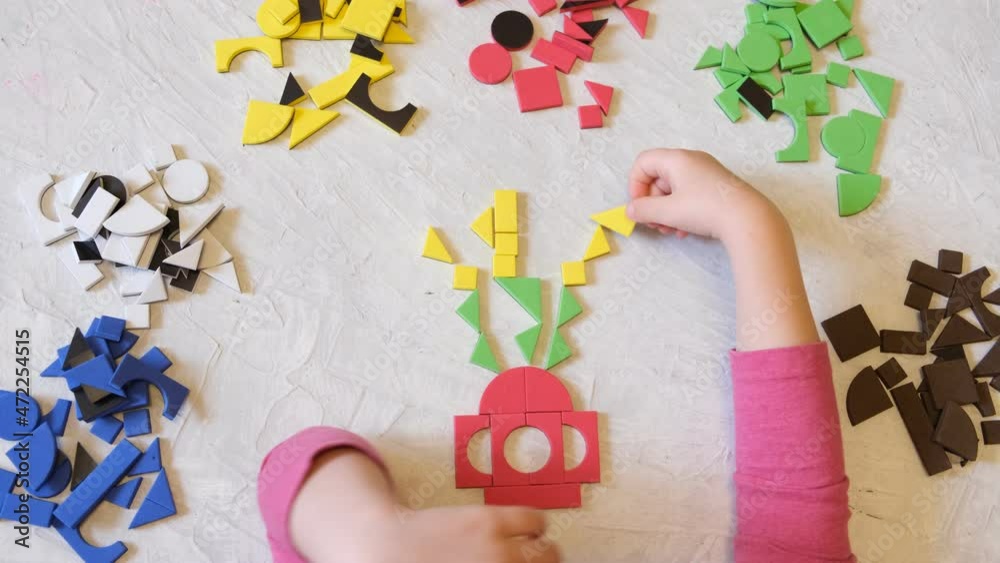 Toddler girl plays with geometric mosaic details. game for creativity.  Leisure of child, development of fine motor skills and abstract thinking.