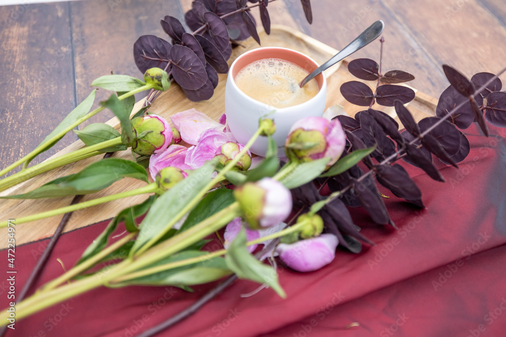 A white Cup of black coffee stands on a wooden background next to pink peonies and other garden flowers and leaves, The concept of village life, Cottagecore, ruralcore, cluttercore. High quality photo A white Cup of black coffee stands on a wooden background next to pink peonies and other garden flowers and leaves, The concept of village life, Cottagecore, ruralcore, cluttercore. High quality photo