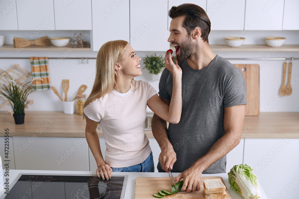 Girl feeding her boyfriend with tomatoe at kitchen Girl feeding her boyfriend with tomatoe at kitchen