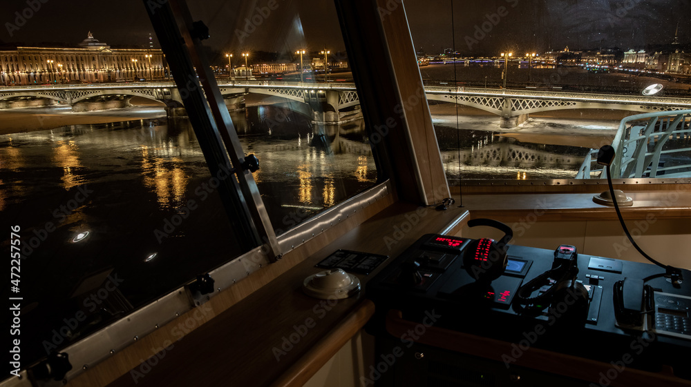 The panoramic view from cabin of ship of the winter night city Saint-Petersburg with picturesque reflection on water, big ship moored near Blagoveshchensky bridge or lieutenant Schmidt
