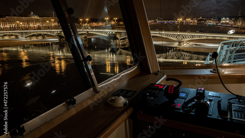 The panoramic view from cabin of ship of the winter night city Saint-Petersburg with picturesque reflection on water, big ship moored near Blagoveshchensky bridge or lieutenant Schmidt