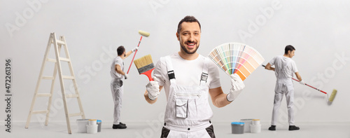 House painter holding a color swatch palette and a brush and other painters painting a wall