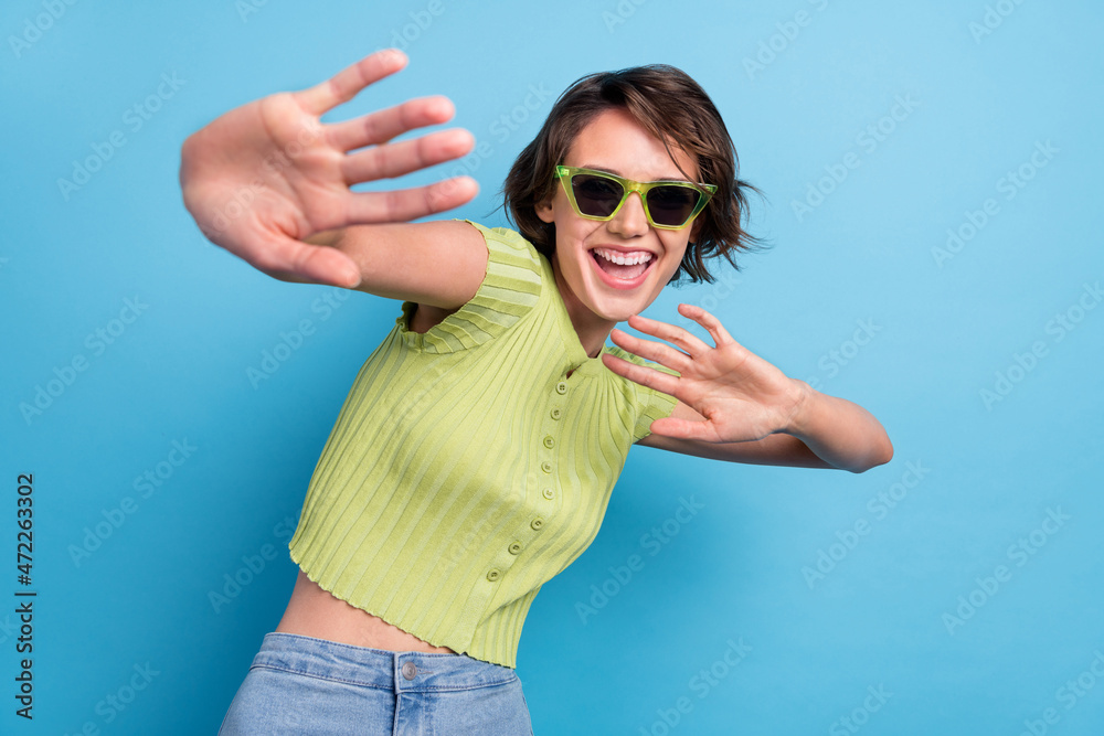 Photo of shiny sweet young woman dressed green t-shirt dark glasses dancing smiling isolated blue color background