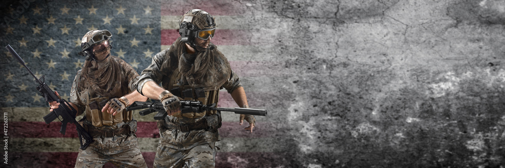 Fototapeta premium Two mercenary soldiers walk after the successful completion of the operation against the background of a concrete wall with an American flag. Format 3x1. Collage - one model, in two poses.