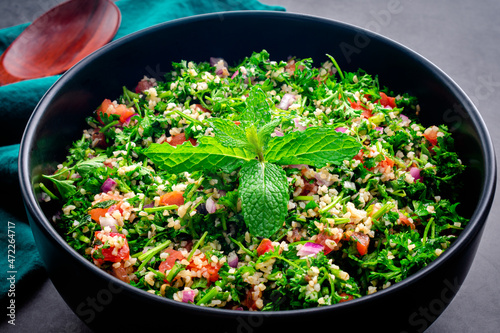 Authentic Lebanese Tabbouleh Garnished with Mint Leaves: A large serving bowl of parsley salad with bulgur wheat, tomatoes, and onions photo