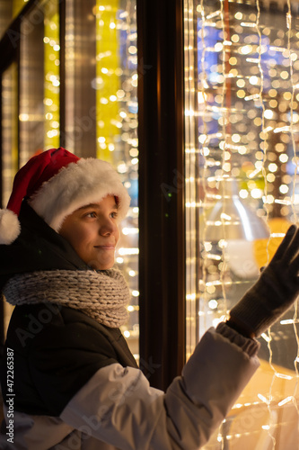 Boy in Santas hat looking and dreaming in illuminated shop window. Xmas presents holidays, or shopping on New Year or Christmas concept © olinchuk