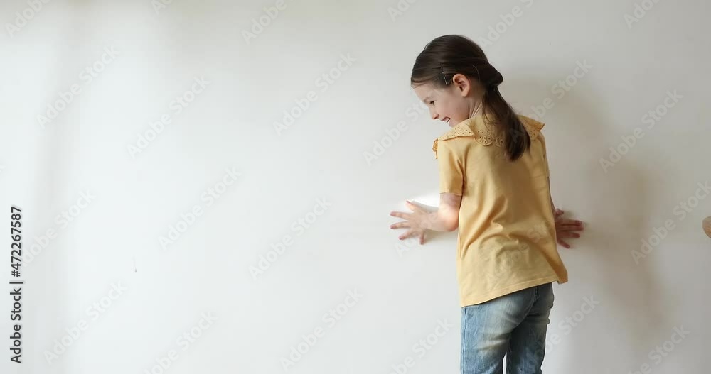 Sweet moments. Back rear view carefree little girl 5 years old playing funny game trying to catch sun twinkle moving on white wall. Preschool child having fun at home enjoy chasing plash of sunlight