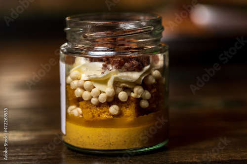 Dessert in a glass tub filled with cream cheese and caramel with white chocolate balls covered with dark chocolate and a crunchy biscuit base