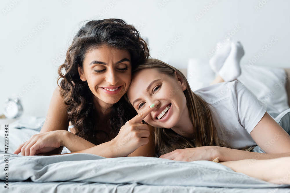 joyful lesbian woman lying on bed and touching nose of girlfriend joyful lesbian woman lying on bed and touching nose of girlfriend