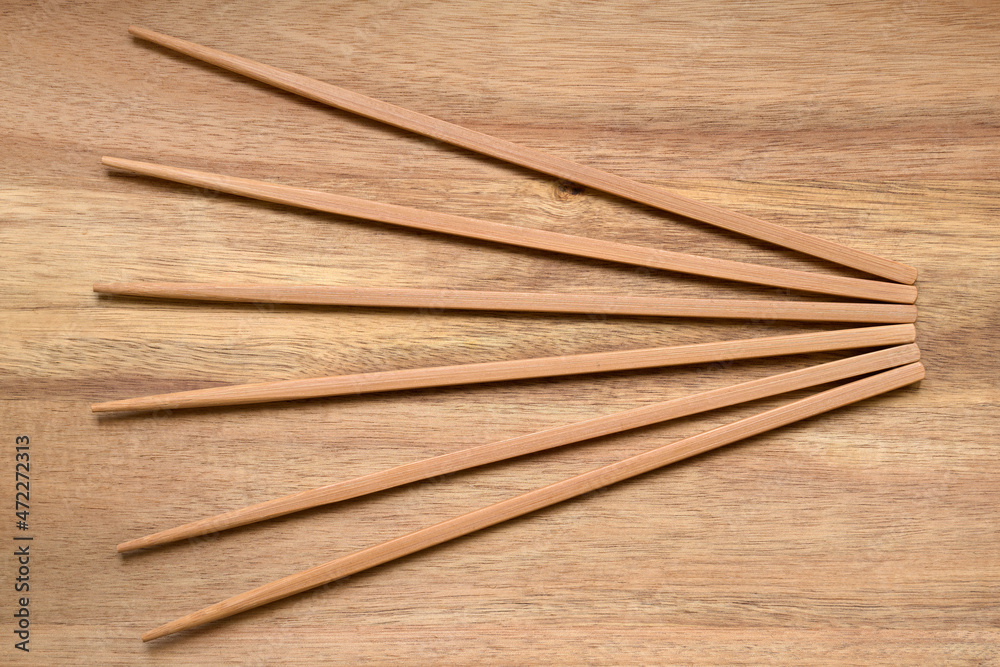 Top view of bamboo chopsticks fanning out against a wooden board, close up