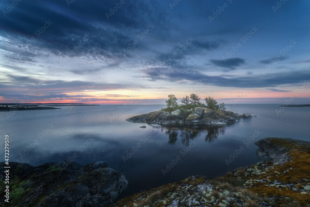 Scenic evening view of a beautiful lake and a lonely rocky island. Epic blue sky. Northern picturesque and harsh nature. Ladoga skerries. Islands. Republic of Karelia. Russia.