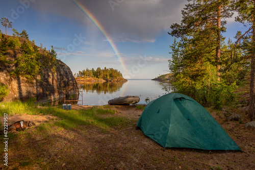 Perfect view of the islands on a sunny early morning with dramatic clouds. A colorful rainbow pierces the blue sky. Green tent and rubber boat foreground. Ladoga skerries. Republic of Karelia photo