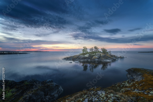 Scenic evening view of a beautiful lake and a lonely rocky island. Epic blue sky. Northern picturesque and harsh nature. Ladoga skerries. Islands. Republic of Karelia. Russia.