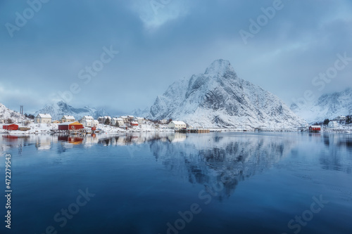 Stunning view of the mountain reflected in the water. Early blue morning in a Norwegian village. Gentle winter sunrise on Lofoten. Beauty of snowy winter nature concept background. Norway. Lofoten. 