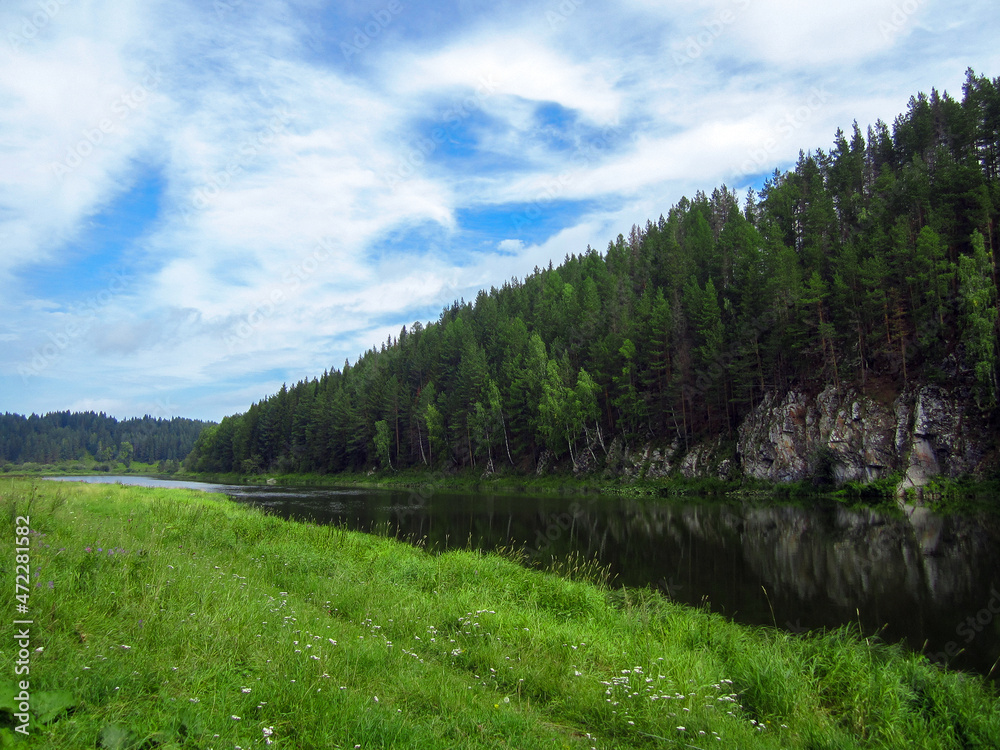 The river against the background of the forest, spruce trees, rocks. Blue sky with clouds. Green glade. The river against the background of the forest, spruce trees, rocks. Blue sky with clouds. Green glade.