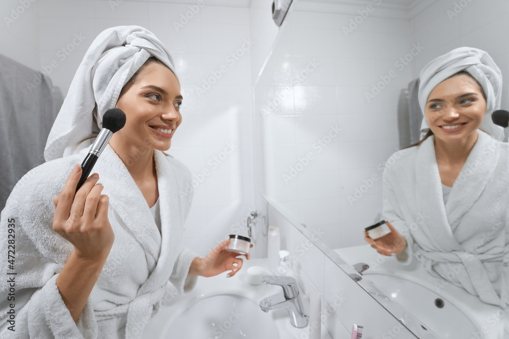 Beautiful woman in white robe looking at himself in the mirror in bathroom. Concept of woman doing makeup. Beautiful woman in white robe looking at himself in the mirror in bathroom. Concept of woman doing makeup.