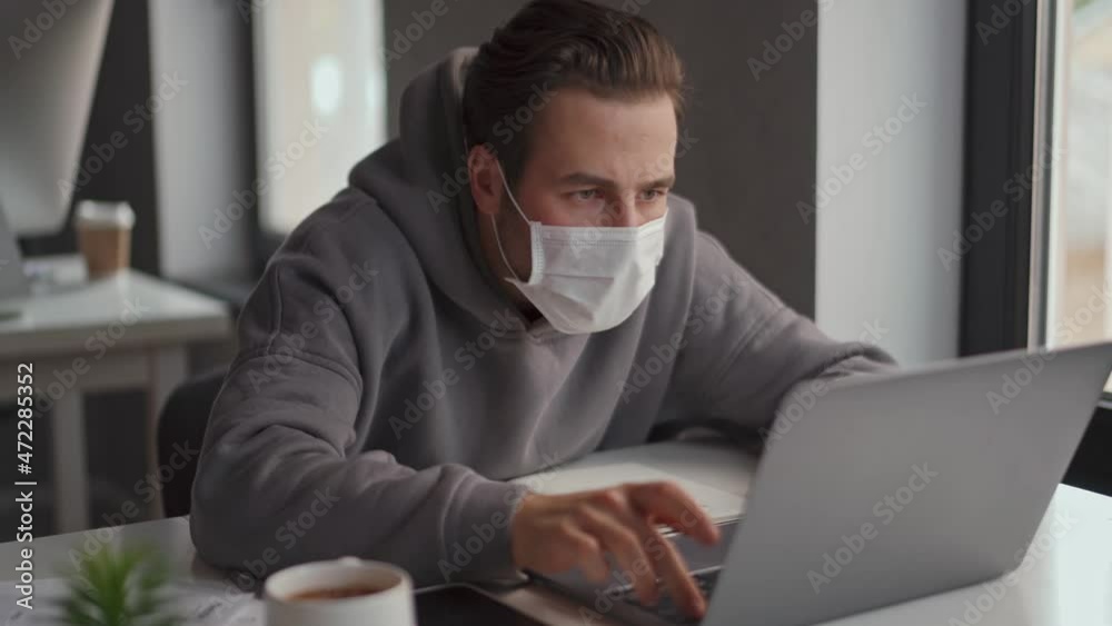 Confident man in protective mask working on laptop in the office Confident man in protective mask working on laptop in the office