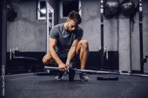 Working out in the gym with no other people, individual training. A shot of a handsome man in a grey shirt and shorts setting up equipment for training in a modern sports center. Fitness challenge