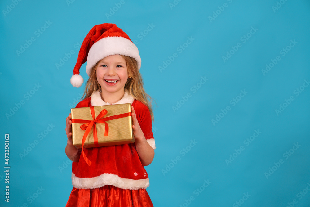 Obraz premium Happy merry Christmas child in Santa hat hold gift. beautiful girl smiles laughs. Congratulate celebration. Jolly Santa Claus preparing box gold red bow. Happy New Year. Place for text. Copy space. 