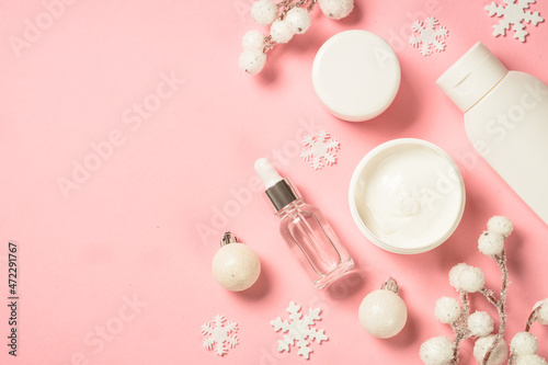 Winter cosmetic, skin care product. Cream, serum, tonic with winter decorations. Top view on pink background with copy space.