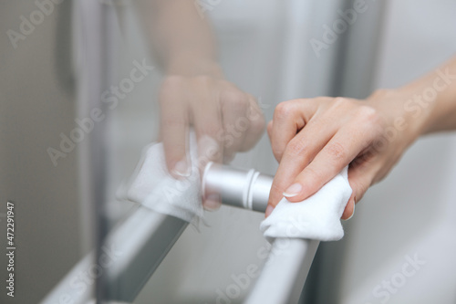 Cleaning glass door handles with an antiseptic wet wipe. Woman hand using towel for cleaning home room door link. Sanitize surfaces prevention in hospital and public spaces against corona virus