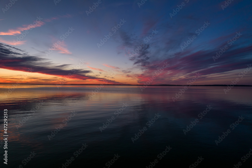 Beautiful sundown over the lake. Blue sky and pastel pink clouds during summer sunset. Mirror image of clouds in the water.