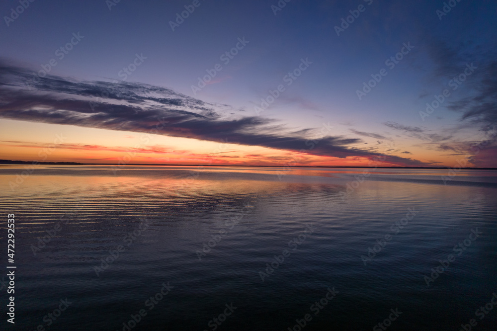 Beautiful sundown over the lake. Blue sky and pastel pink clouds during summer sunset. Mirror image of clouds in the water. Beautiful sundown over the lake. Blue sky and pastel pink clouds during summer sunset. Mirror image of clouds in the water.