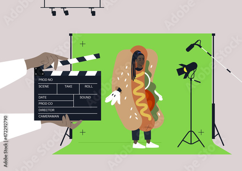 A young female African character wearing a hot dog costume at the commercial filming, a chroma key screen, lighting equipment, a microphone, a clapper board