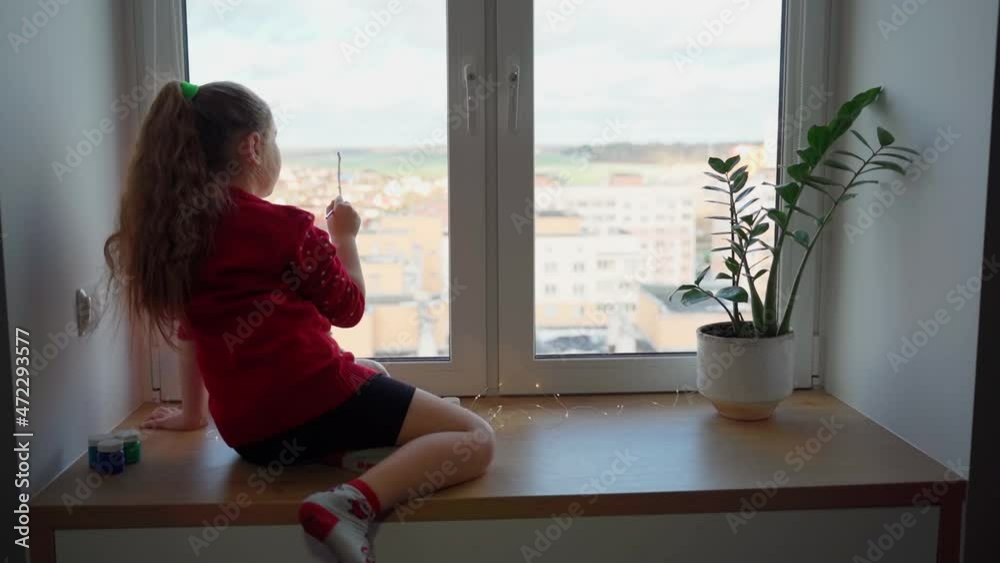 Child begin draw snowflake on window with paint. Female person school age using paints to decorate her room for christmas holidays. Pretty girl having fun indoors. New year traditions. Slow motion Child begin draw snowflake on window with paint. Female person school age using paints to decorate her room for christmas holidays. Pretty girl having fun indoors. New year traditions. Slow motion