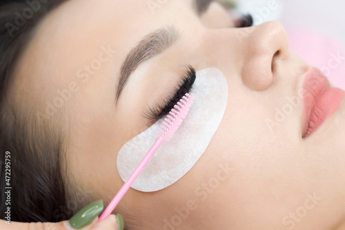Beautiful girl with long artificial eyelashes. Eyelash extension procedure. Pink brush combs eyelashes.