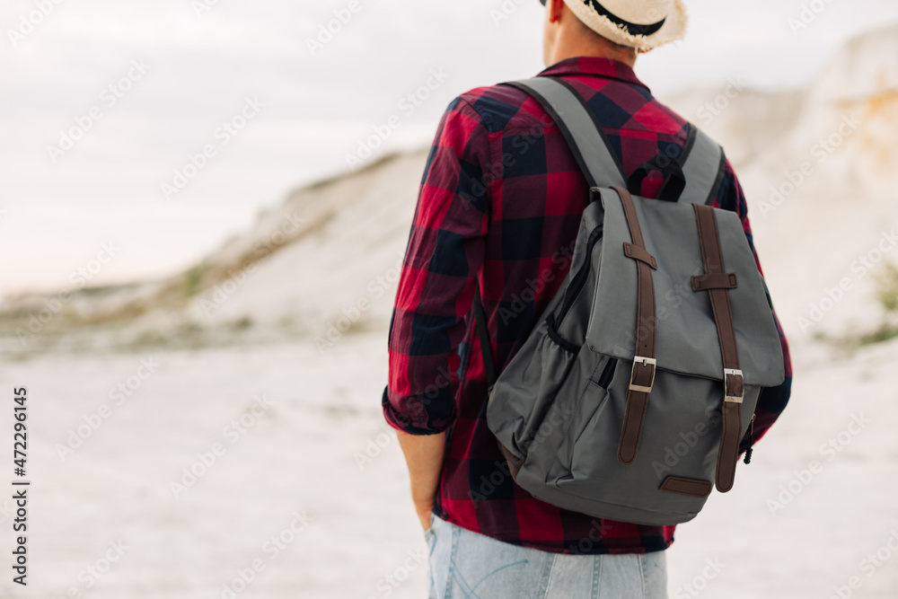 Male hipster traveler with backpack in hat looking forward to amazing mountains and valleys view Male hipster traveler with backpack in hat looking forward to amazing mountains and valleys view