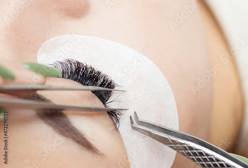 Eyelash extension procedure. The master uses tweezers to apply long eyelashes to beautiful female eyes.
