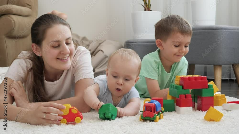 Cheerful smiling family enjoying playing toys and having fun on carpet together at home. Concept of family having time together and children development Cheerful smiling family enjoying playing toys and having fun on carpet together at home. Concept of family having time together and children development