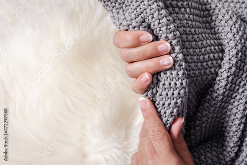 A woman grabbing a grey blanket over a white carpet. French manicure. Copy space.