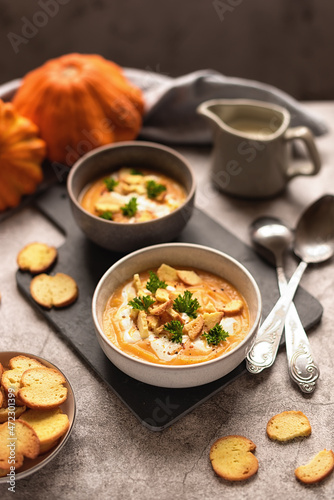 autumn lunch: pumpkin cream soup with cream and crackers. serving lunch for two. photo on gray background
