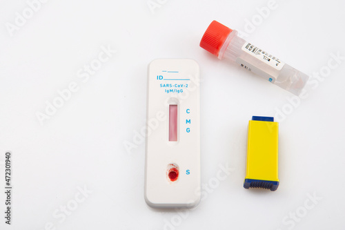 isolated shot of a rapid express antigen antibody coronavirus covid-19 pandemic test sample with blood, a lancet vial and a solution on white background
