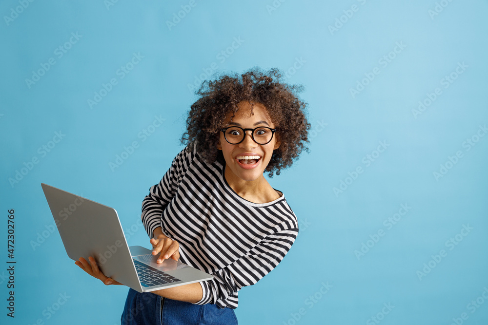 Joyful multiracial lady in glasses looking at camera and laughing while holding notebook. Isolated on blue background Joyful multiracial lady in glasses looking at camera and laughing while holding notebook. Isolated on blue background