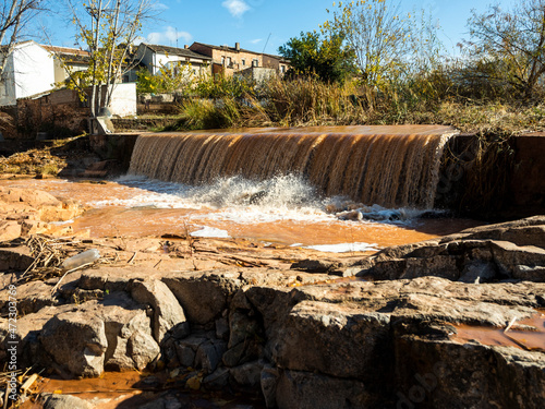 Fotografie cascada de agua marrón con piedras y el cielo azul