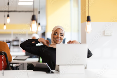 African american muslim girl with hijab working on a laptop in an office.. © Nikola Spasenoski