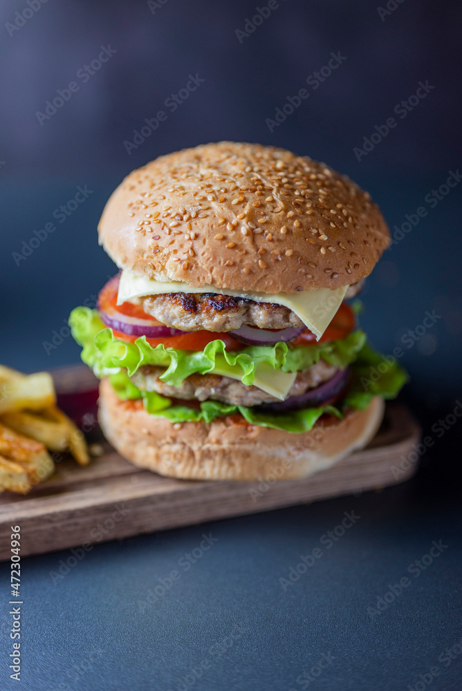 delicious large double burgeon with vegetables cutlet veal meat with lettuce and cheese on a wooden board .Hamburger with fries delicious large double burgeon with vegetables cutlet veal meat with lettuce and cheese on a wooden board .Hamburger with fries
