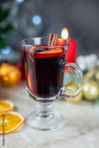 delicious hot spicy red mulled wine with orange and cinnamon spices near the Christmas tree with decorations and bokeh garlands