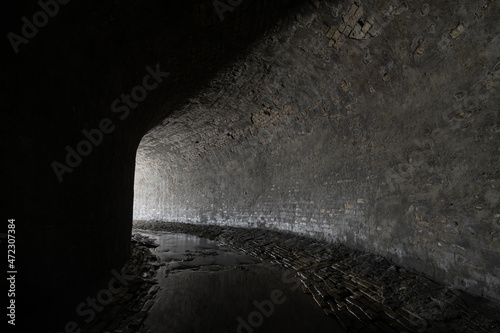 Old brickwork sewer tunnel with light from the turn. Underground river or old rainwater collector of the 19th century.